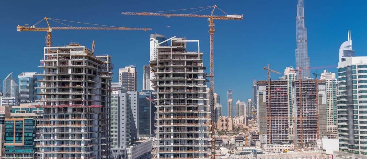 High-rise buildings under construction in Dubai with tower cranes and Burj Khalifa in the background