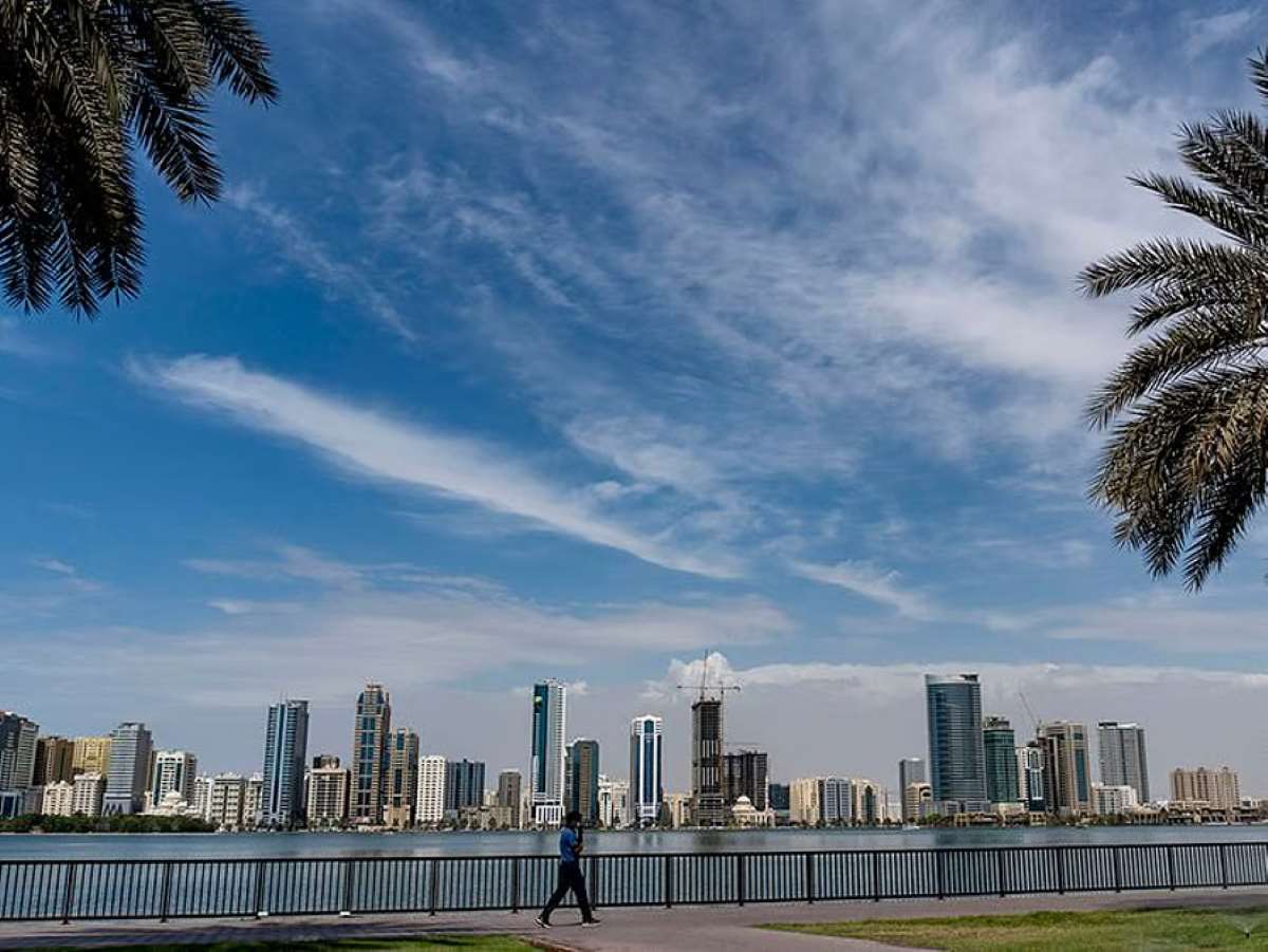 Sharjah skyline with high-rise buildings along waterfront under blue sky with scattered clouds